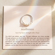 Silver ring with pearls on a card with motivational text about resilience.